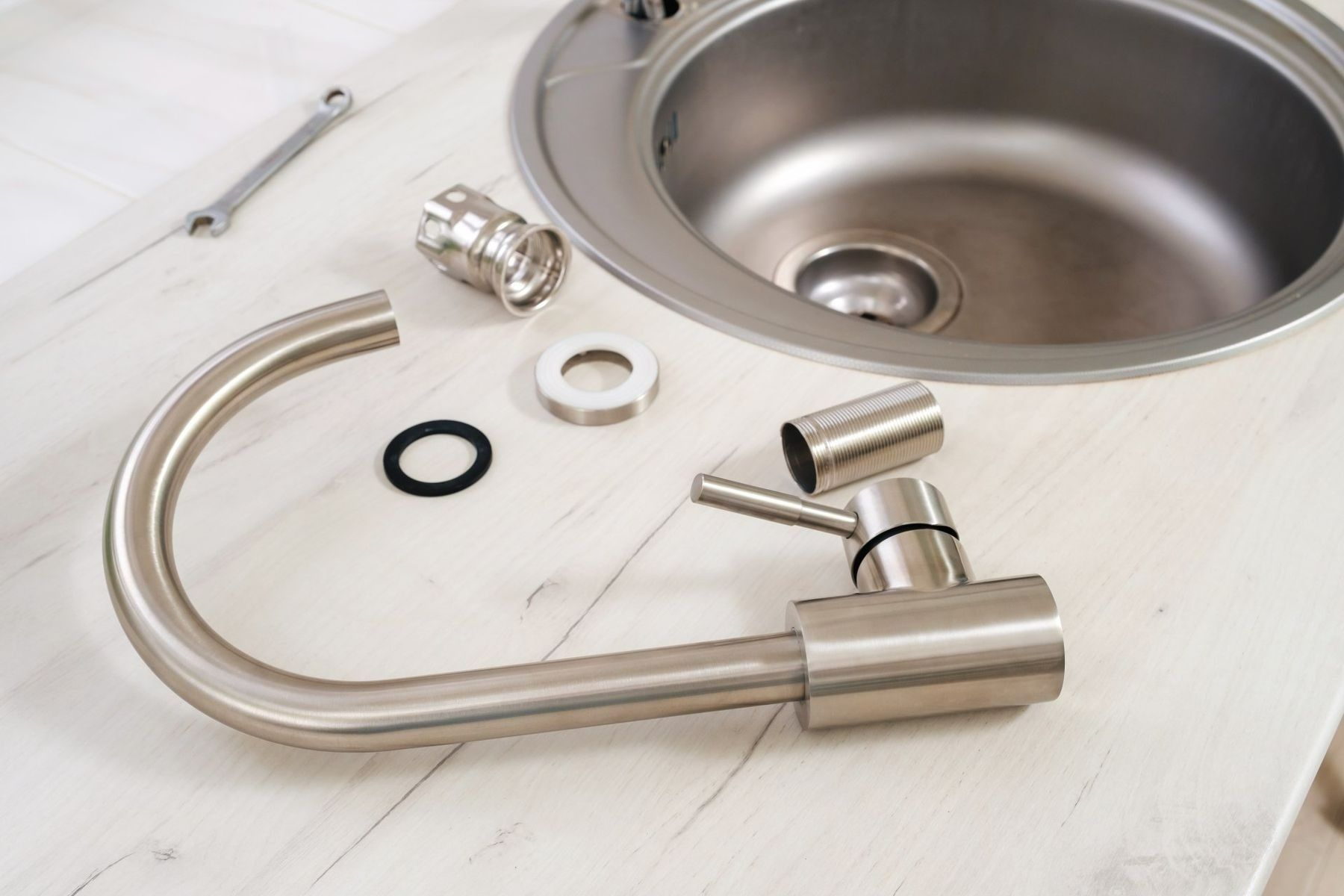 Stainless steel kitchen faucet and parts laid out beside a sink on a light wood surface.