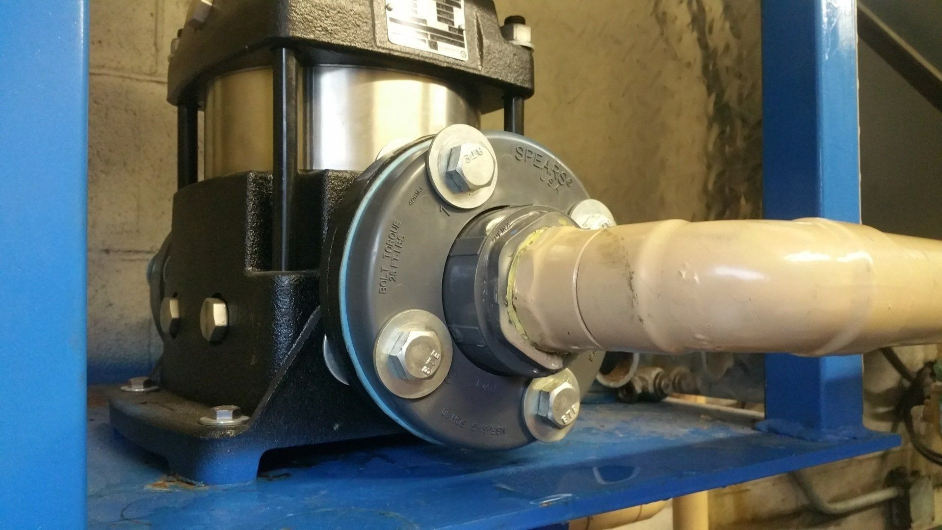 Close-up of a black pump bolted to a blue metal frame, connected to a beige pipe with white tape.