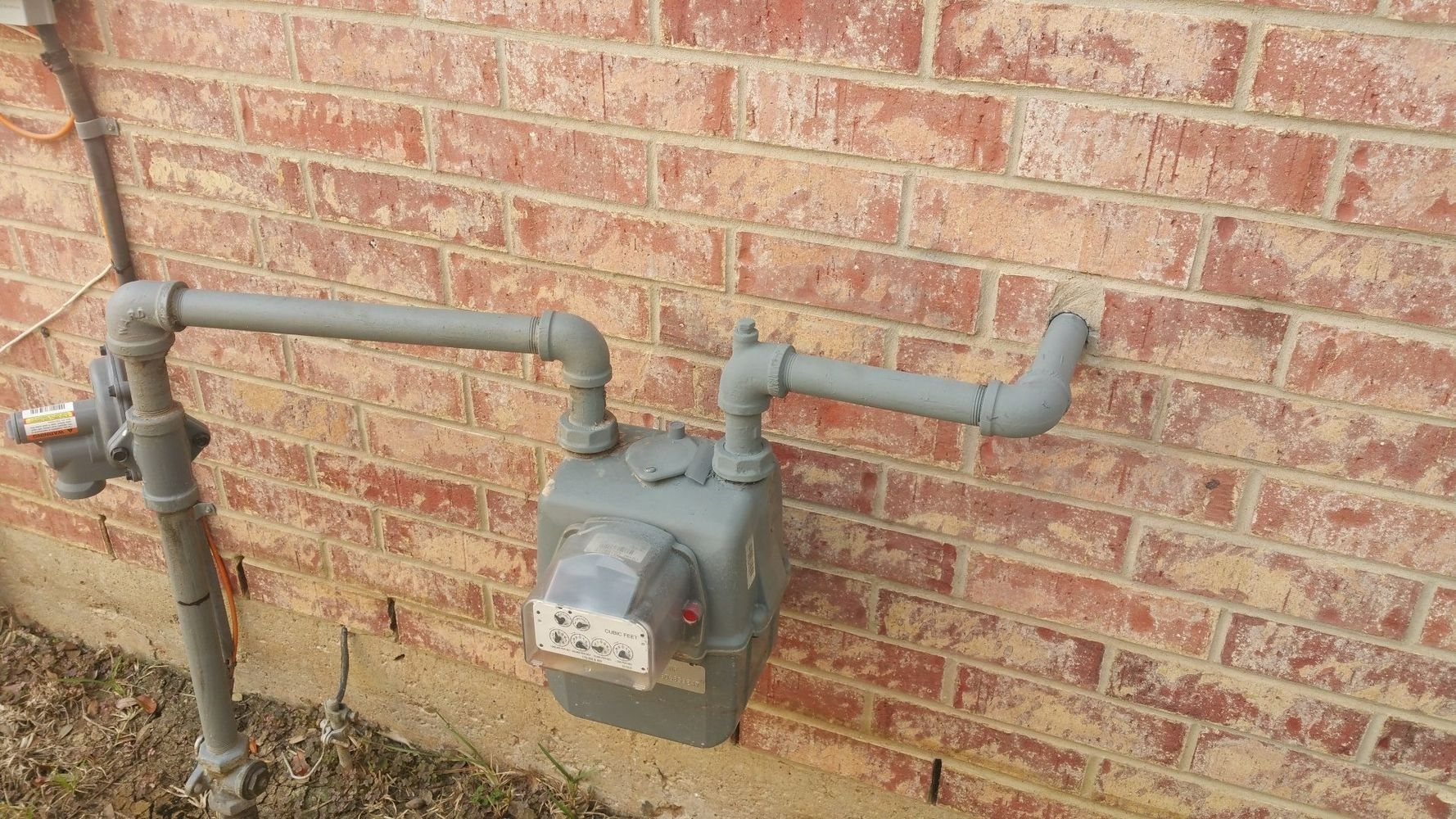 Gas meter on a red brick wall, with gray pipes.