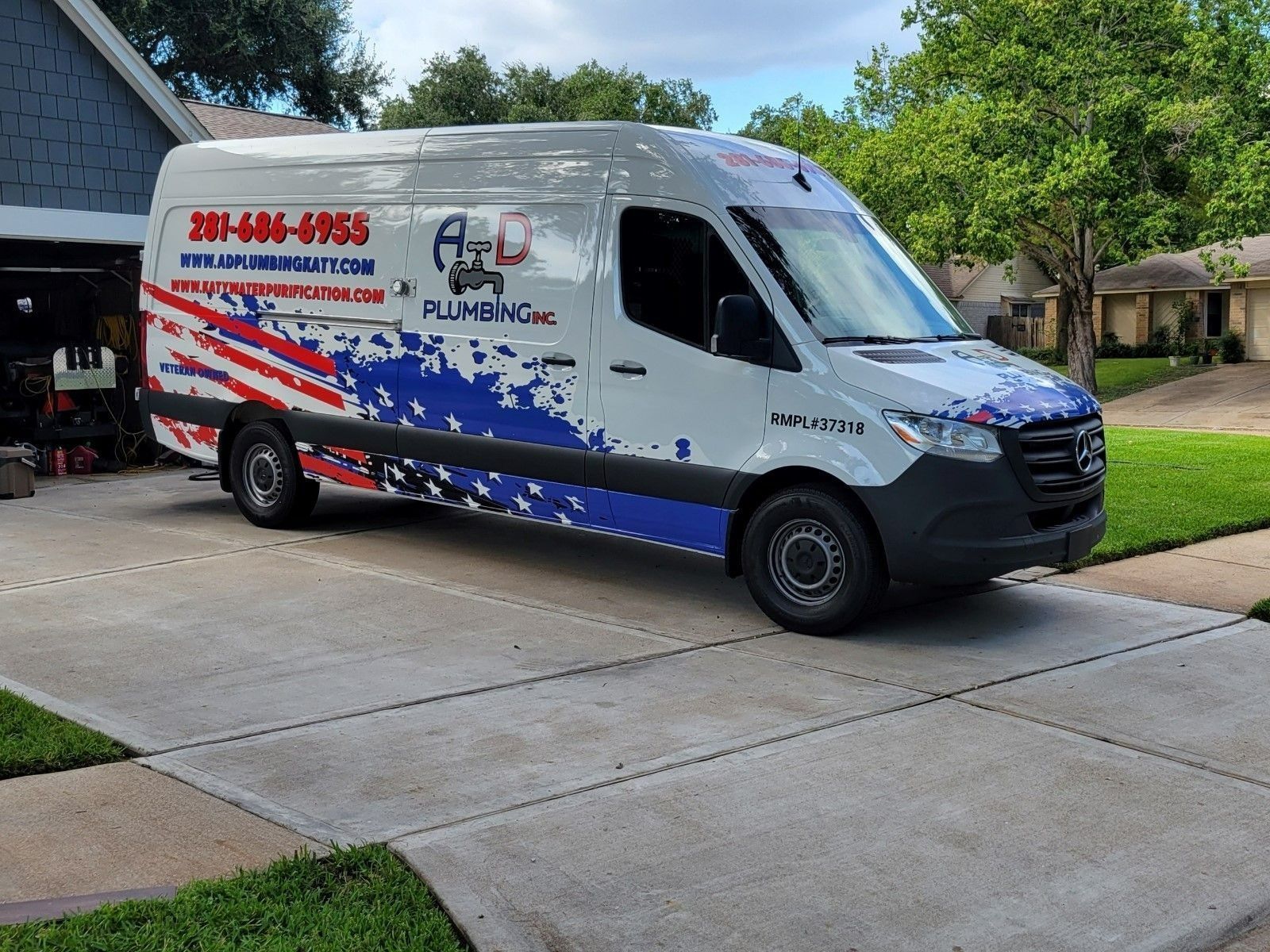 Plumbing service van parked in a driveway; patriotic design with red, white, and blue colors, phone number visible.