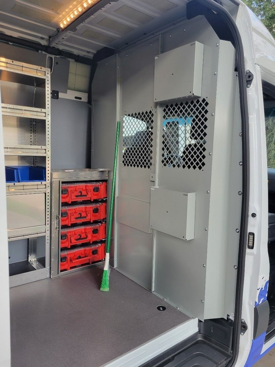 Interior of a work van, featuring storage shelves, red tool boxes, and a partition with a window.