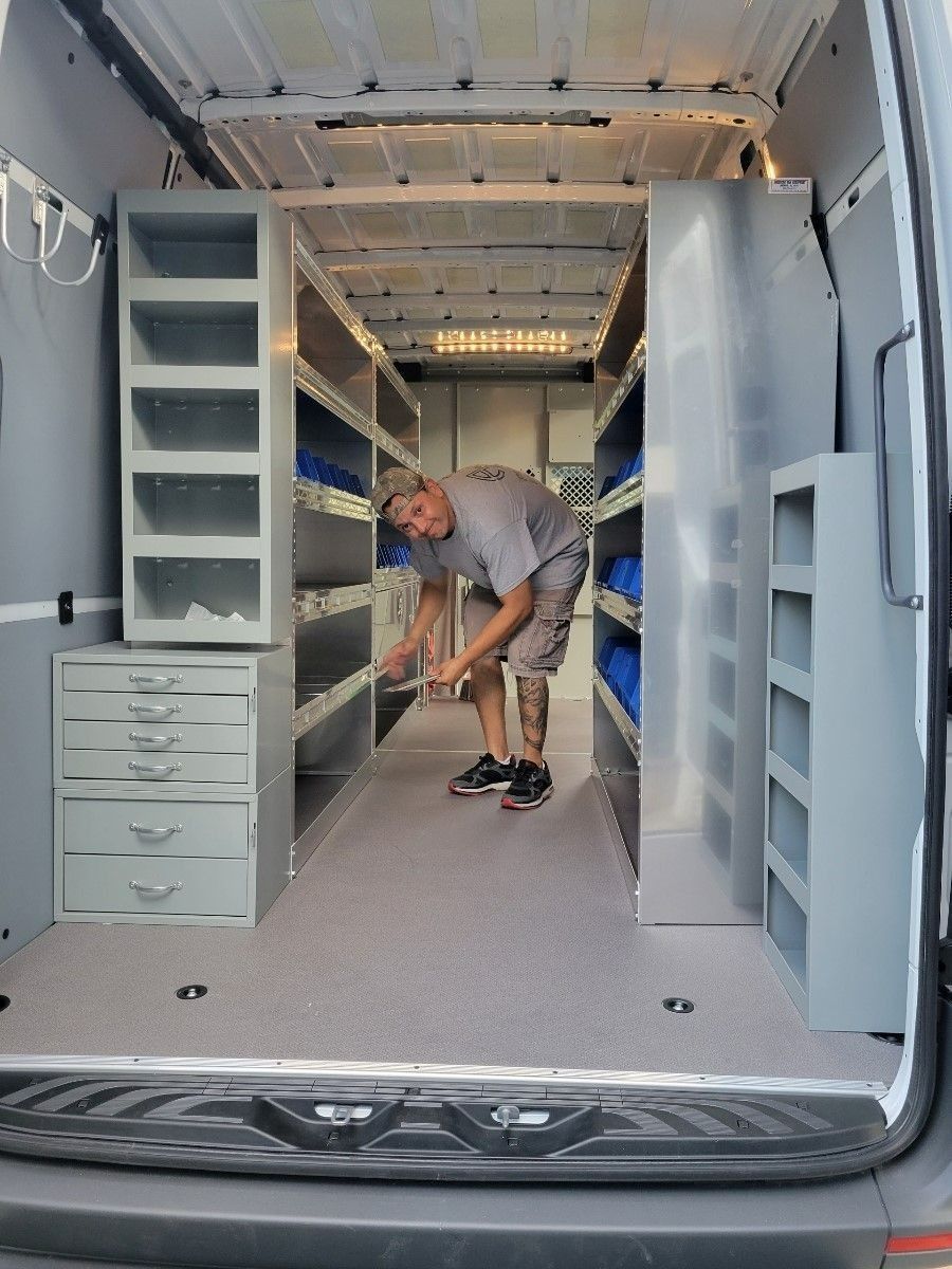 Man in a cargo van, surrounded by shelving units. He is inside the van.