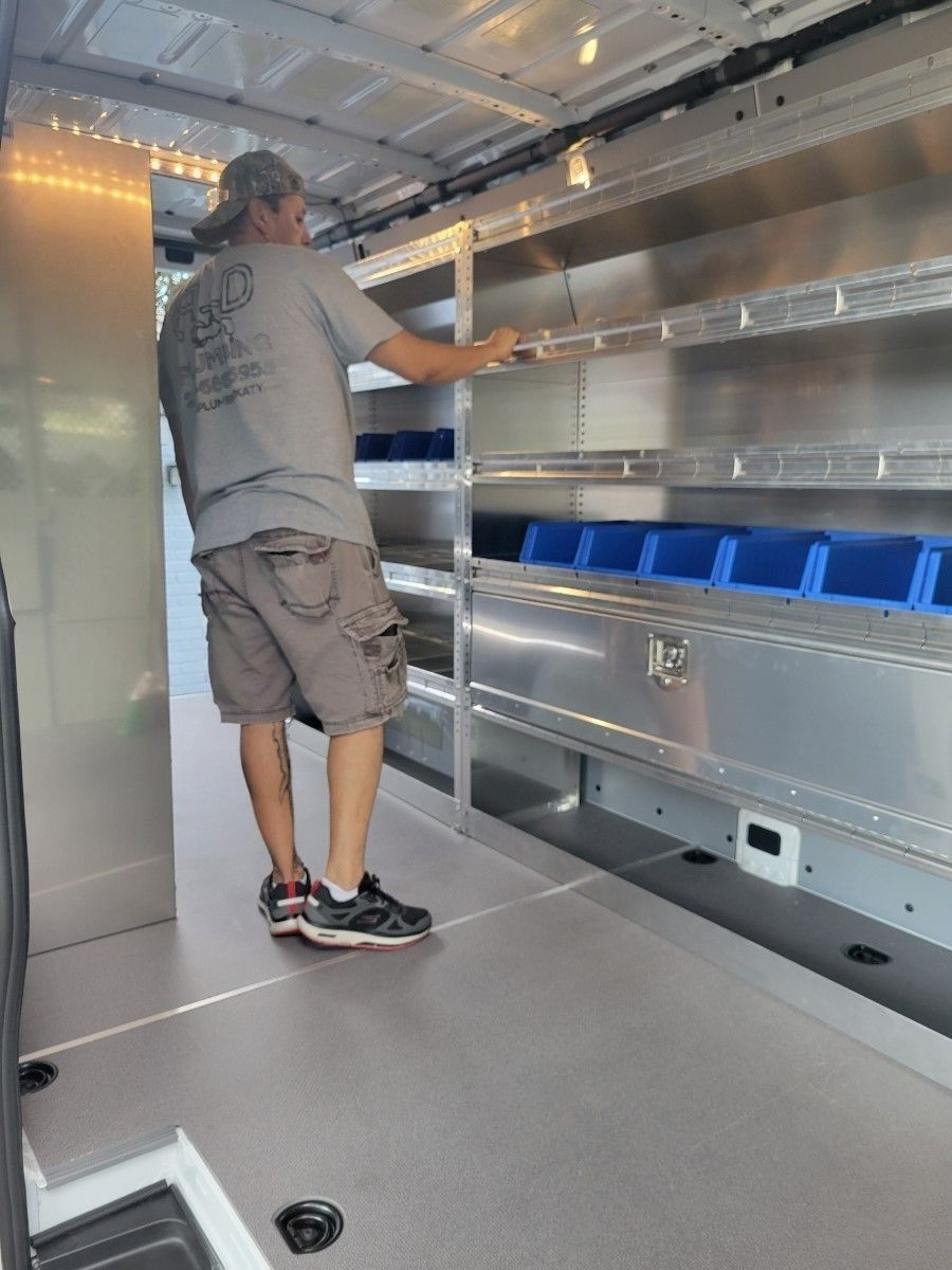 Man inside a van with shelving, touching a shelf. The van interior has gray flooring and metal shelving with blue bins.