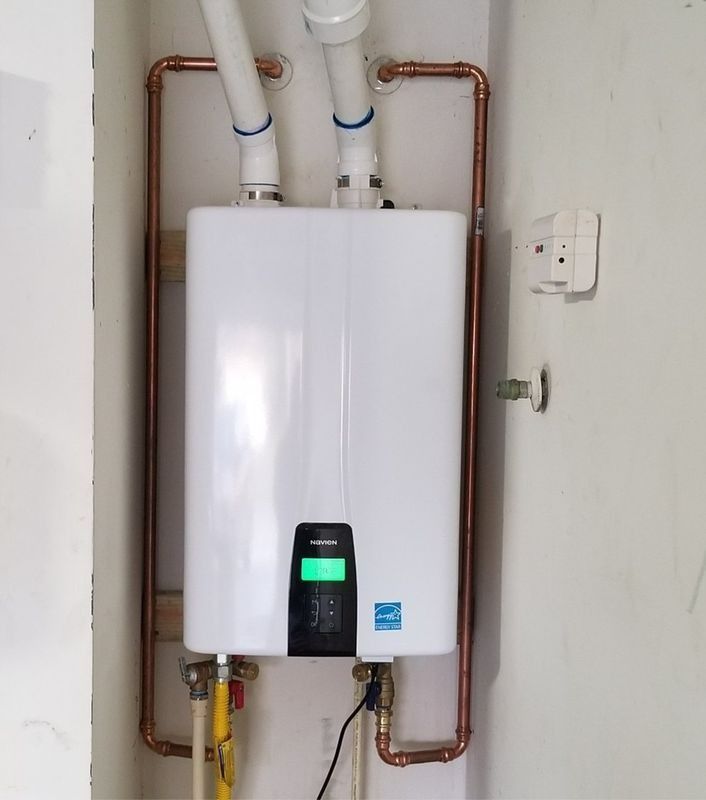 White wall-mounted water heater with copper pipes, gas line, and digital display.