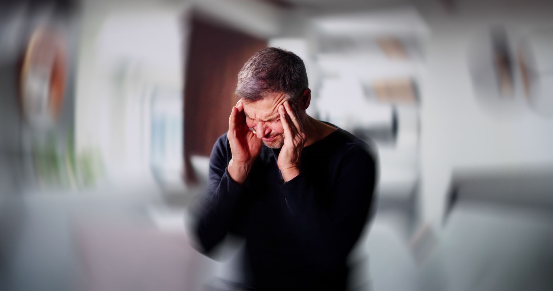 Man with hands on head, eyes squeezed shut, appearing to have a headache. Blurred background.