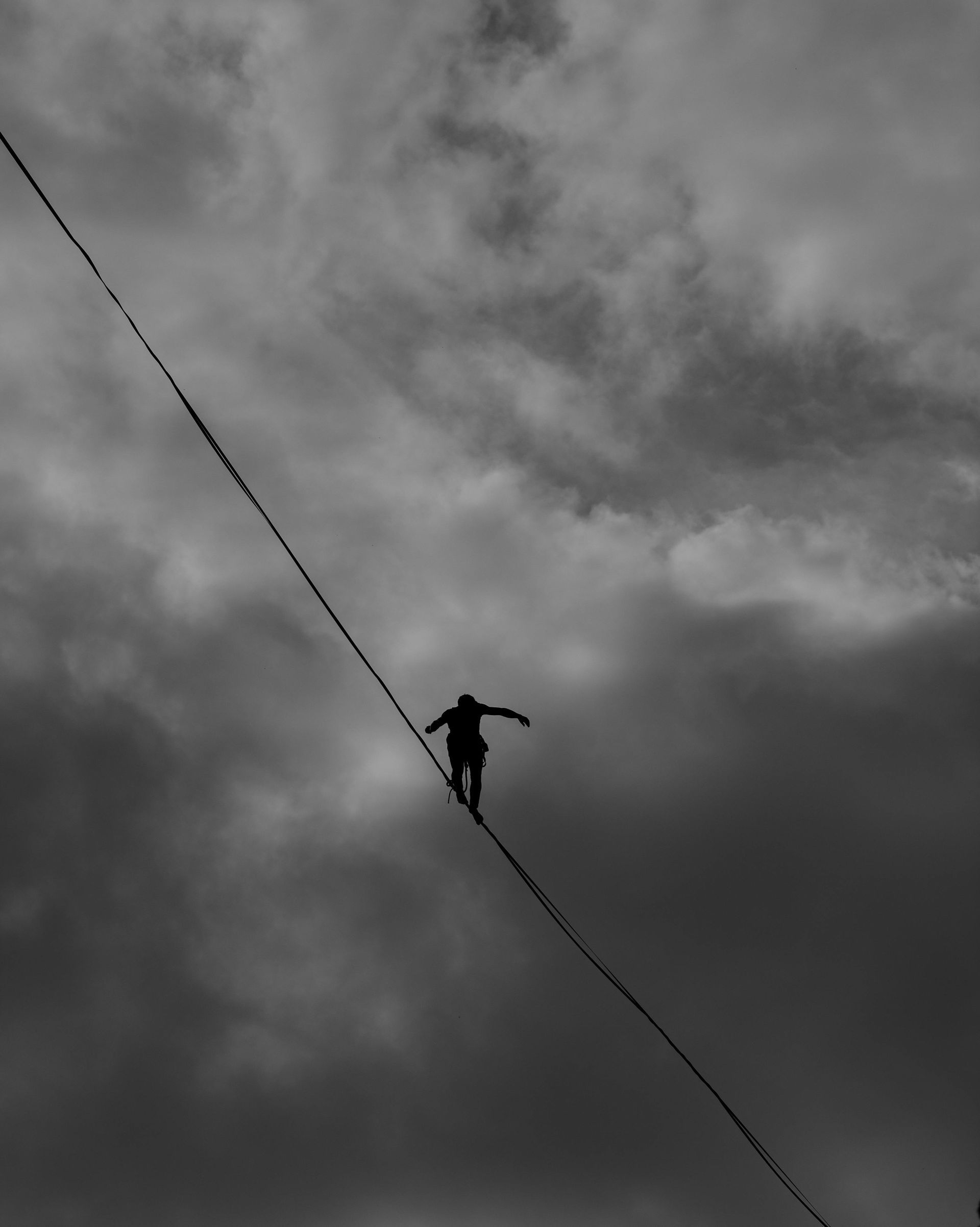 Silhouette of person balancing on a tightrope high above a cloudy sky. Arms outstretched for balance.