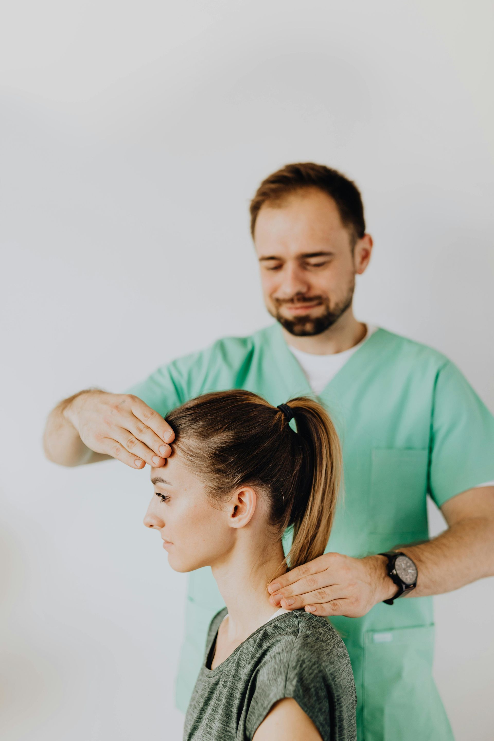 A healthcare professional in a green uniform examining a patient's head and neck.