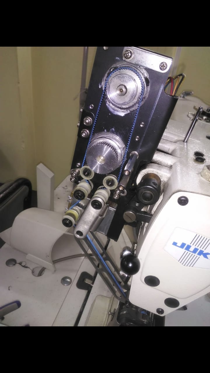 Cabezal de una máquina de coser industrial Juki, que muestra carretes de hilo, correas y mecanismos, en un taller.