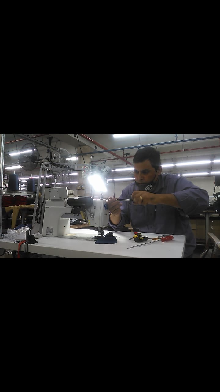 Hombre reparando maquinaria en una estación de trabajo; entorno interior de fábrica; utilizando herramientas, expresión concentrada.