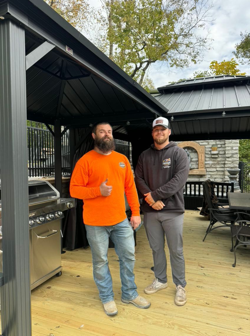 Two men standing on a deck near a gazebo and grill. One in orange gives a thumbs up.