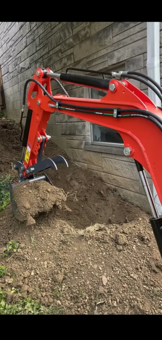 An orange excavator digging a trench beside a weathered wall.