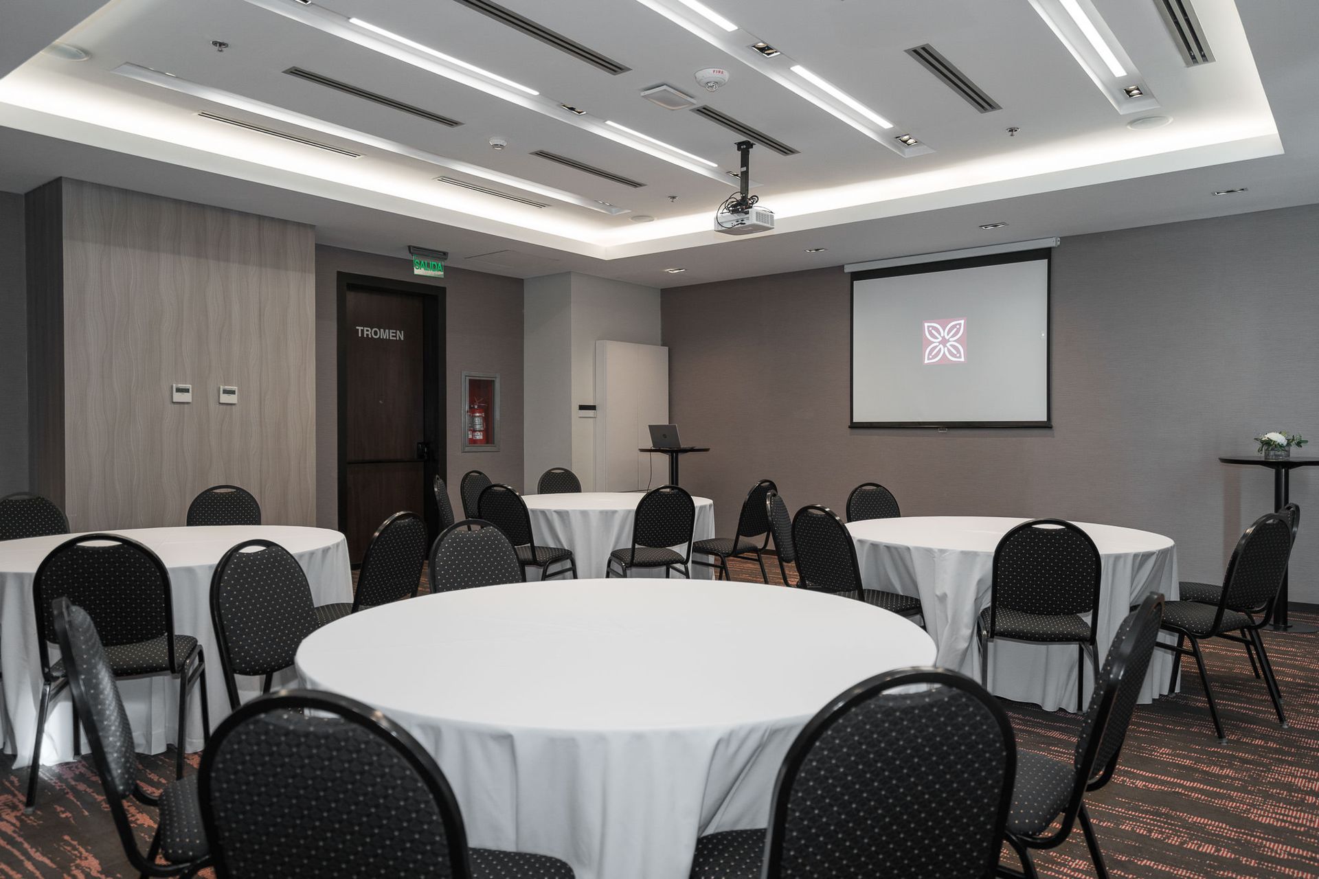 Una sala de conferencias con mesas y sillas y una pantalla de proyección.