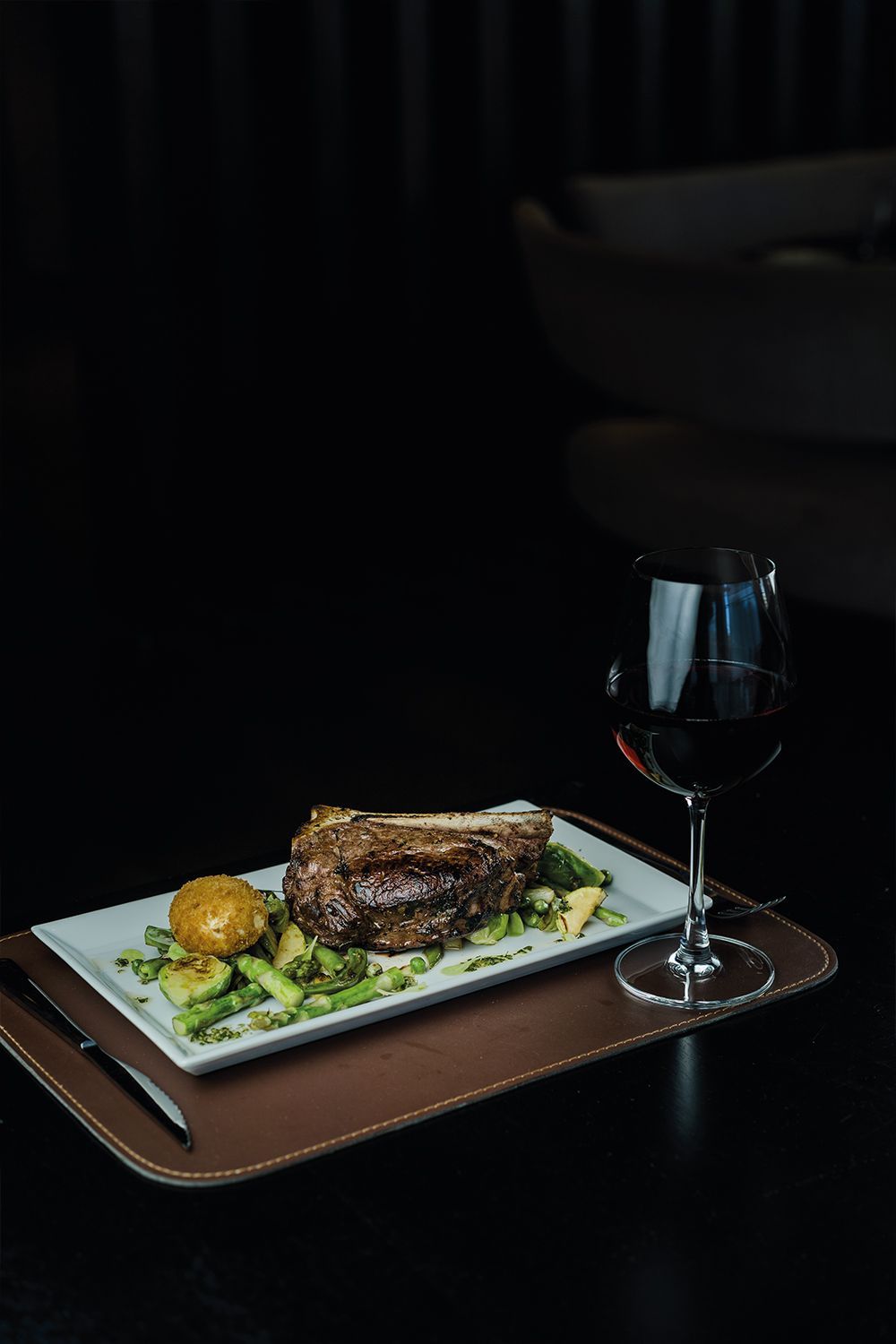 Un plato de comida y una copa de vino en una bandeja sobre una mesa.
