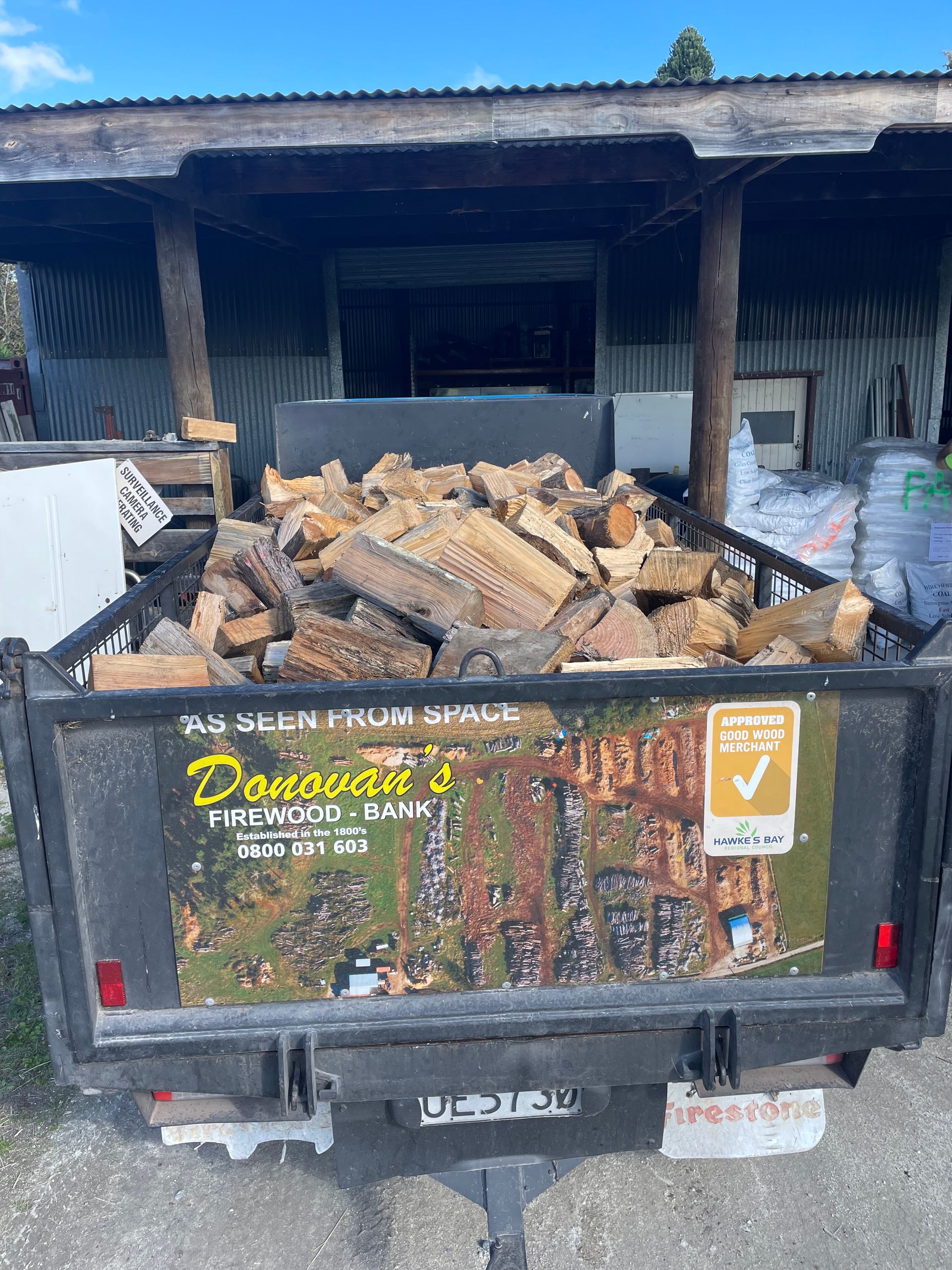 A trailer filled with logs is parked in front of a building.
