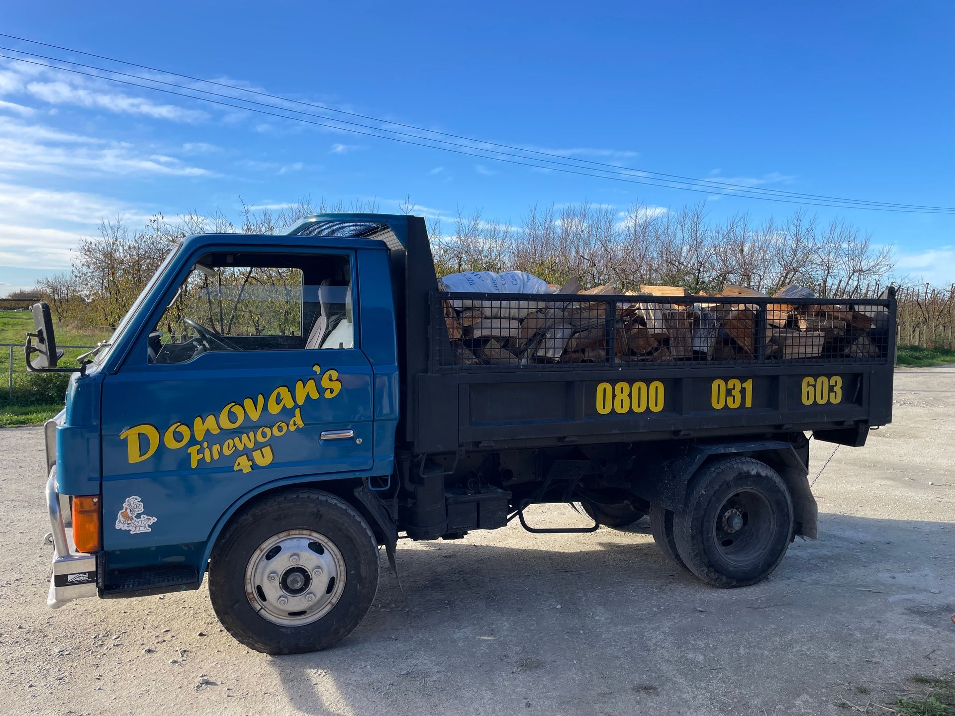 A blue donovan 's firewood truck is parked on a dirt road.