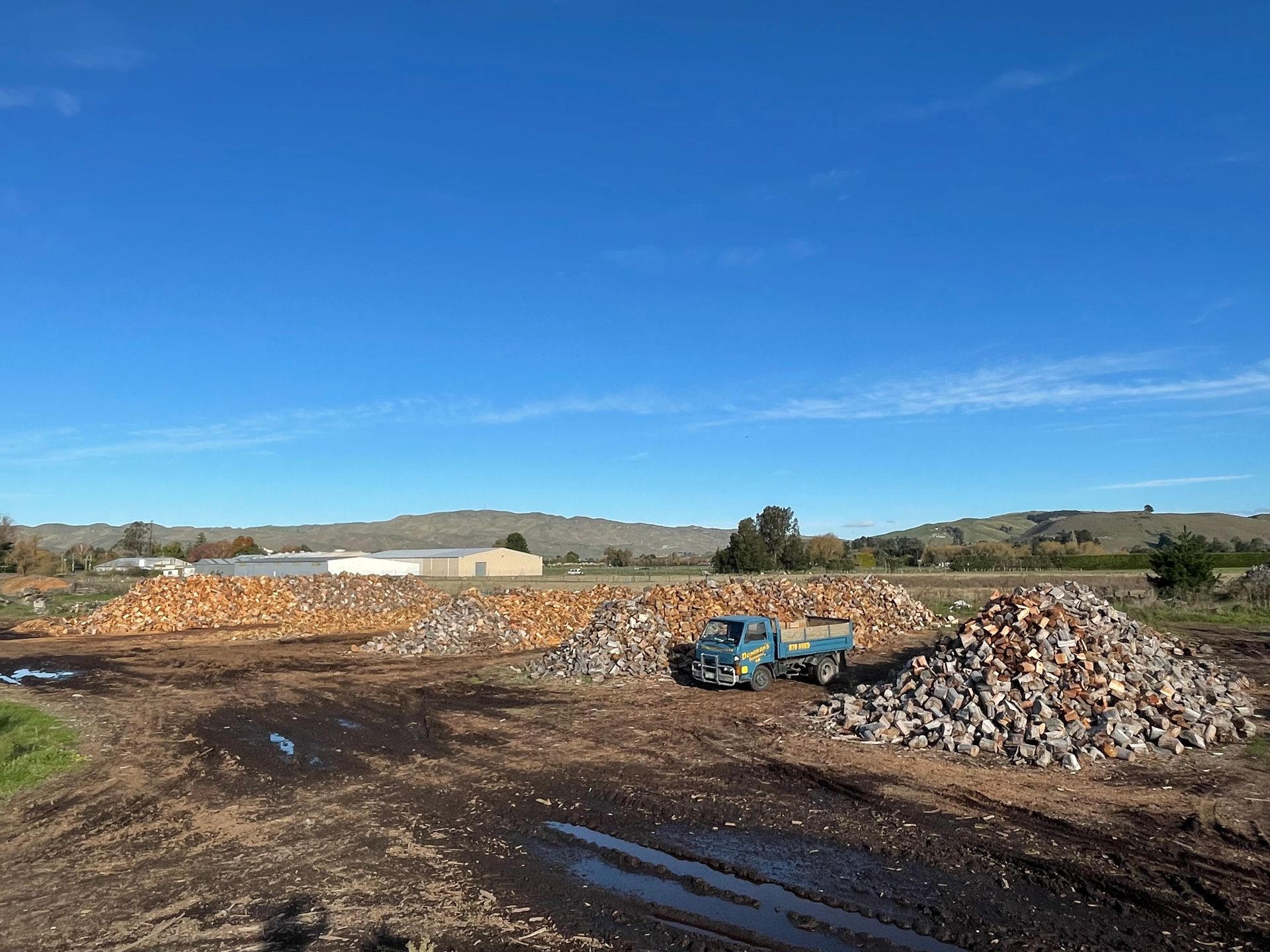 A truck is driving down a dirt road next to a pile of rocks.