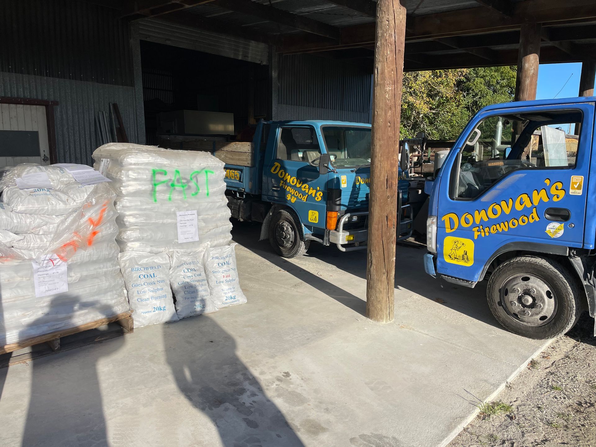 A blue donovan 's firewood truck is parked next to a pile of bags.