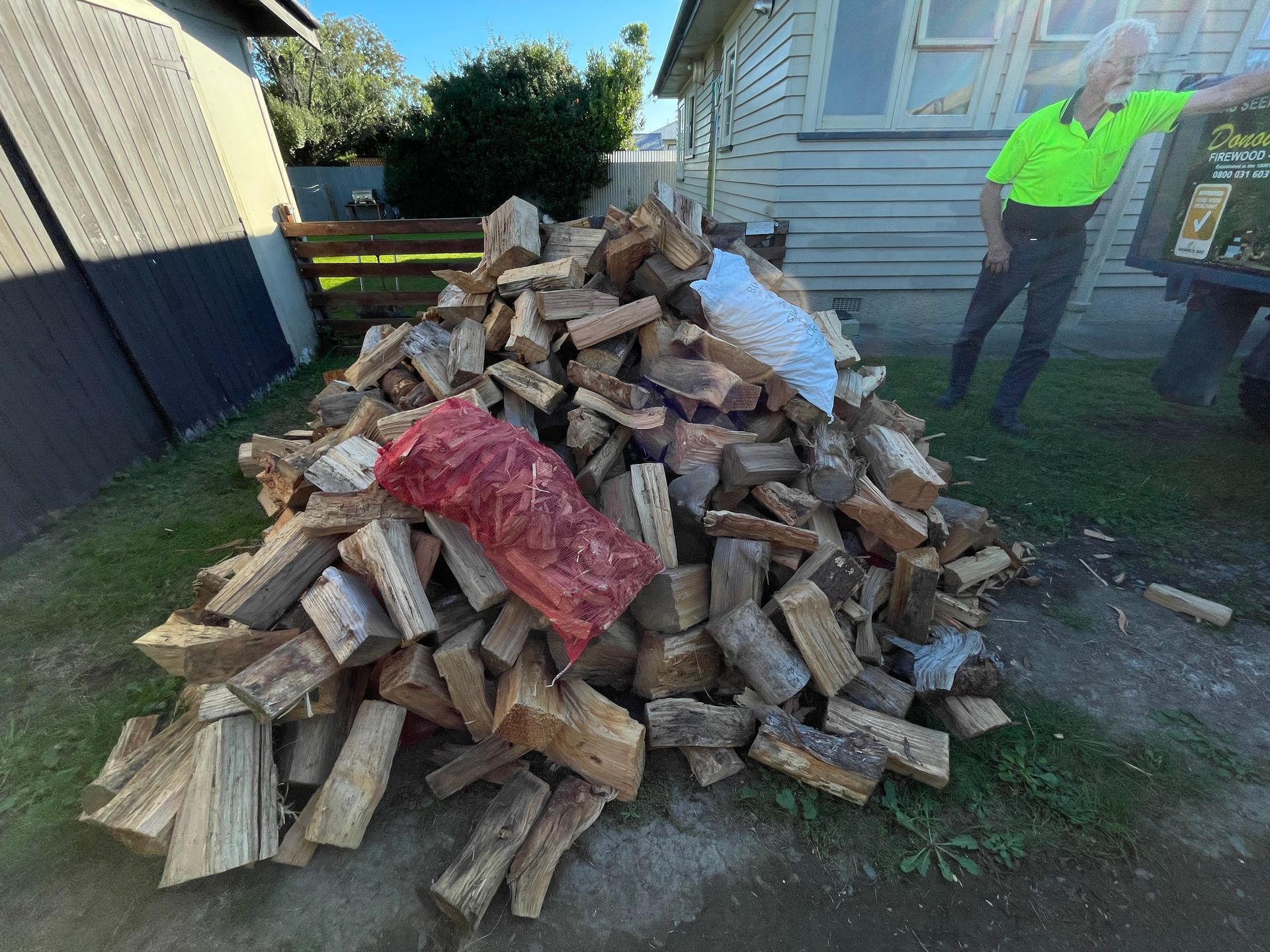 A man is standing next to a pile of wood.