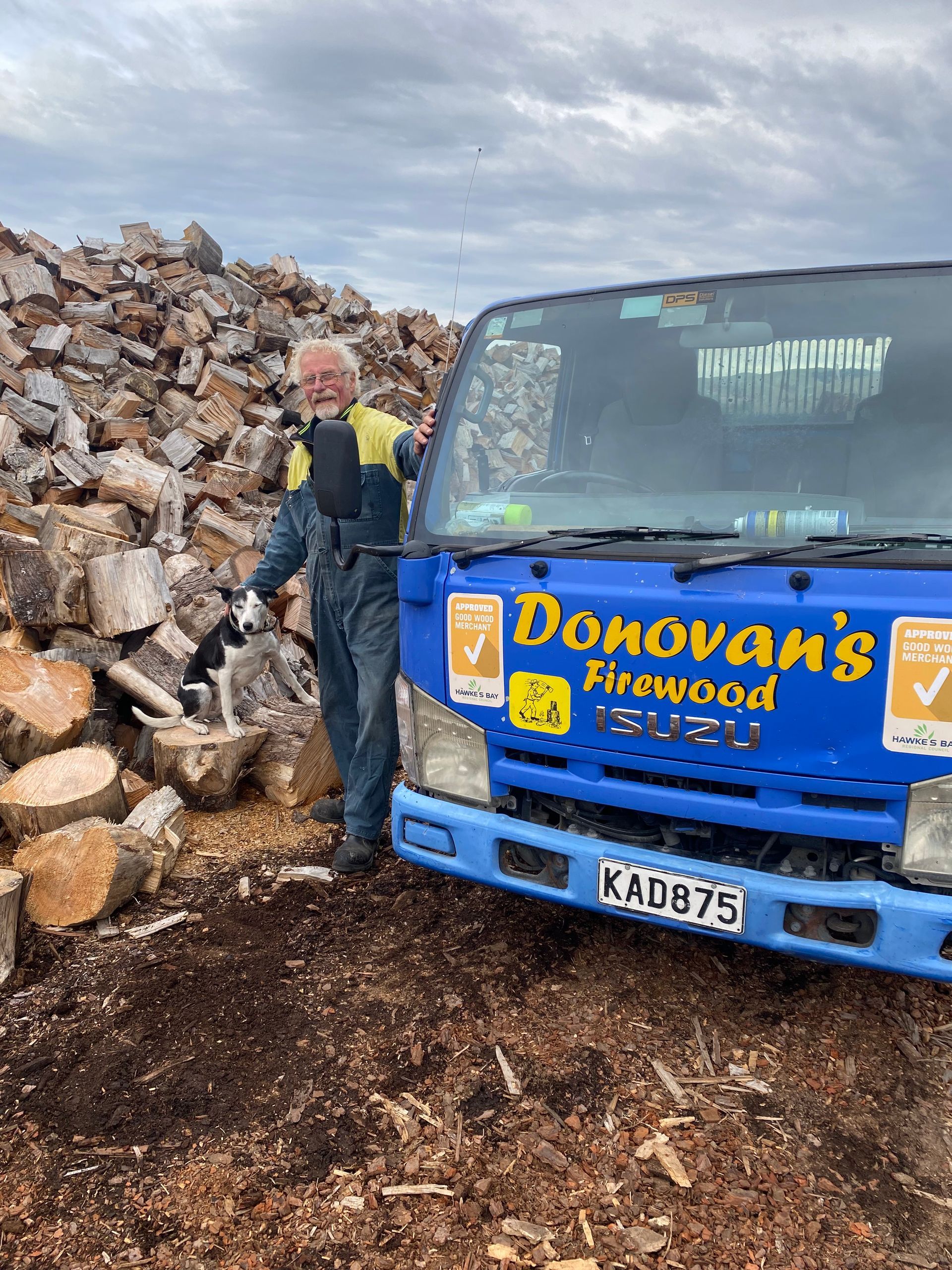 A man is standing next to a blue donovan 's firewood truck.