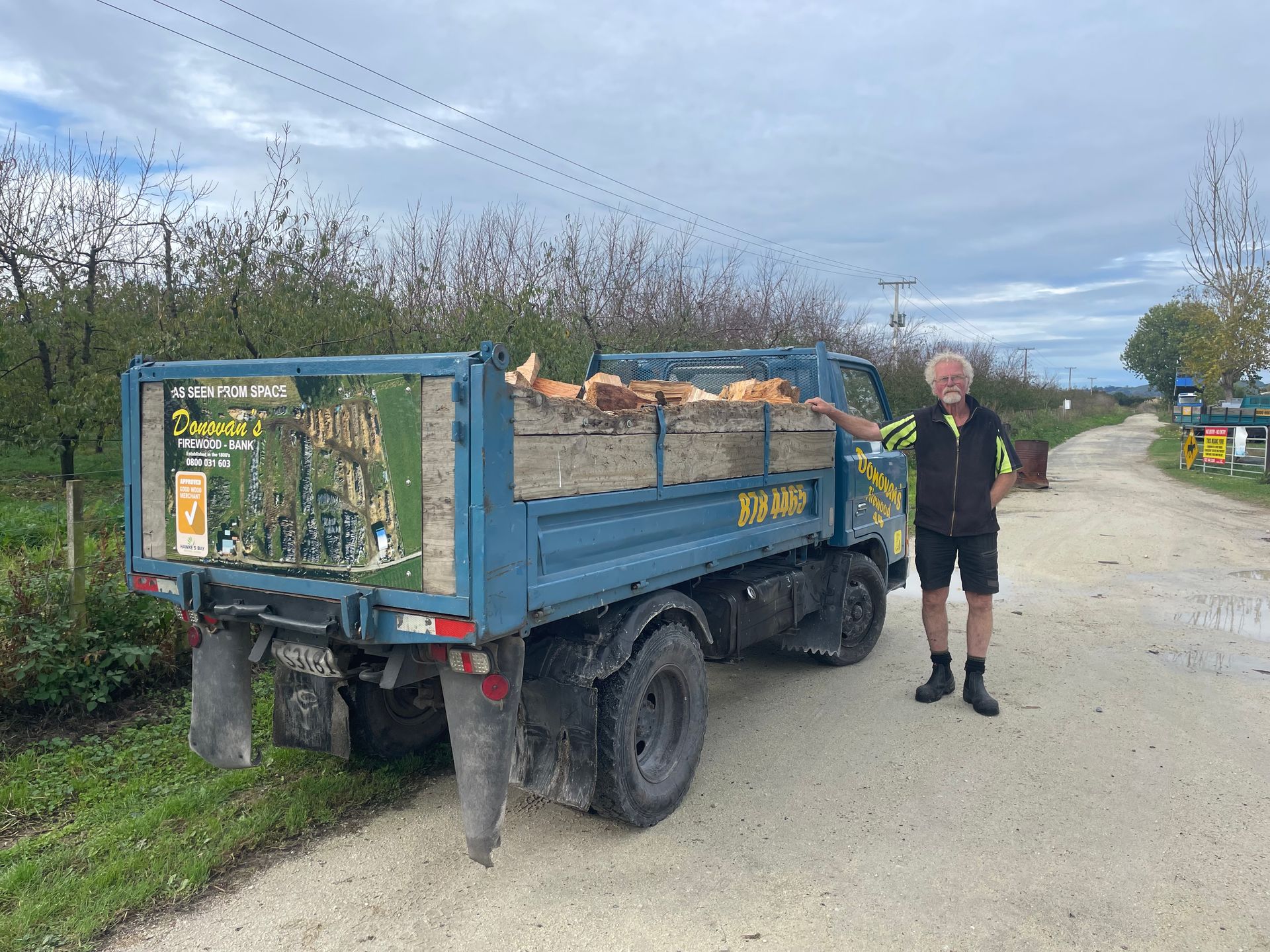 A man is standing next to a blue dump truck on a dirt road.