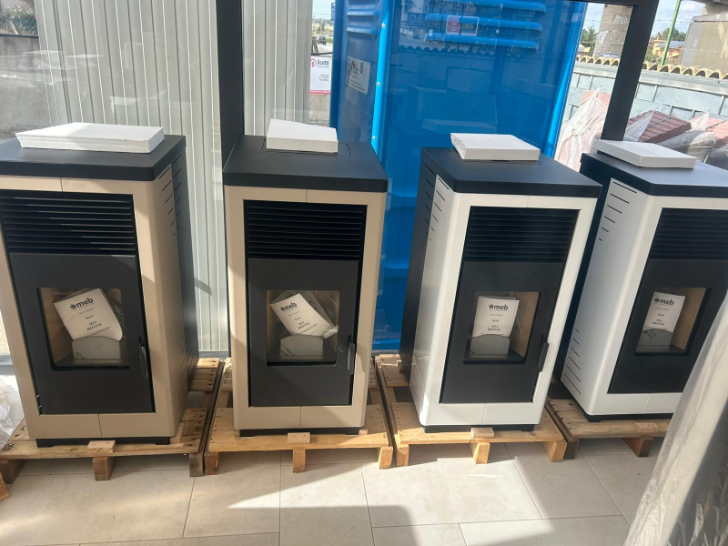 Quattro stufe a pellet di diversi colori esposte vicino a una finestra.