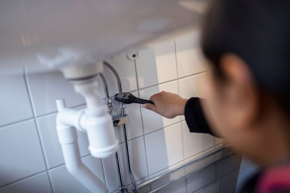 Persona che utilizza una chiave inglese per lavorare sull'impianto idraulico sotto un lavandino bianco.