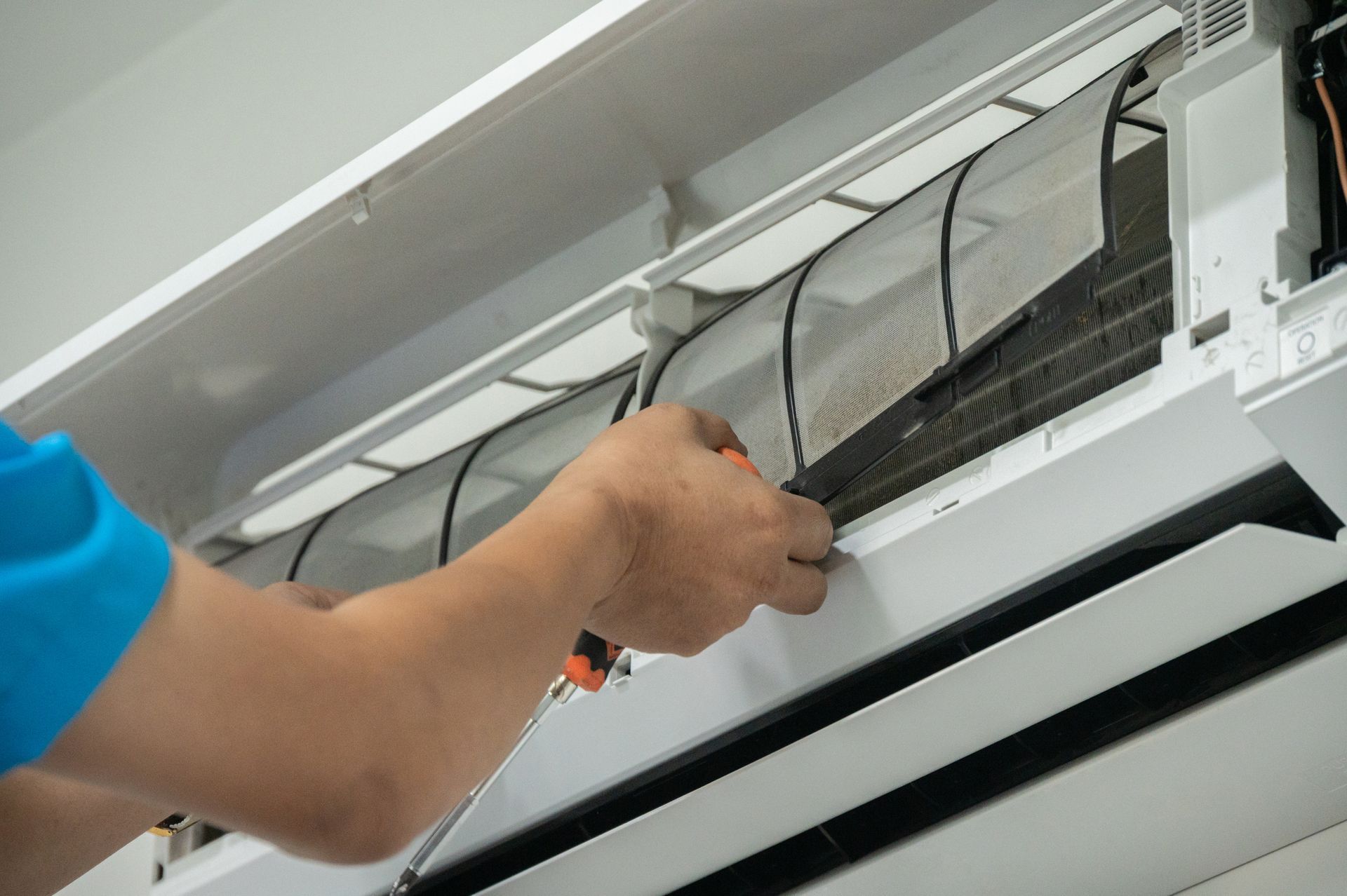 Persona che pulisce il filtro del condizionatore con un cacciavite.