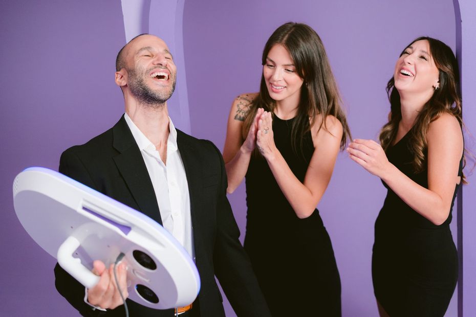 A man in a suit is holding a mirror in front of two women.