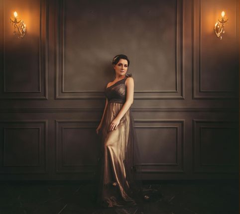 A woman in a long dress is standing in front of a wall.