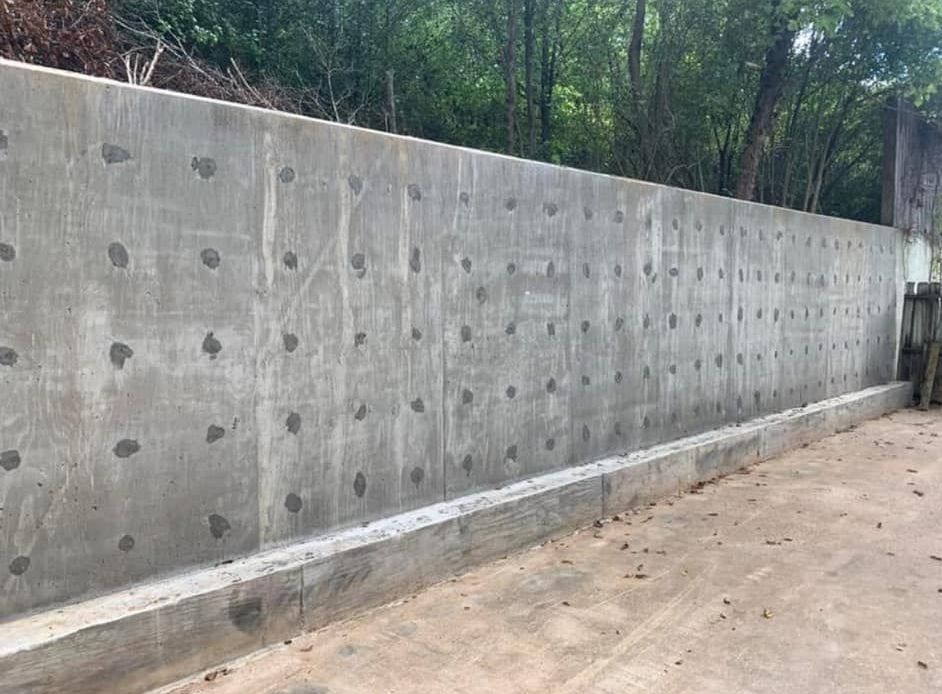 A large concrete wall with holes in it is surrounded by trees.