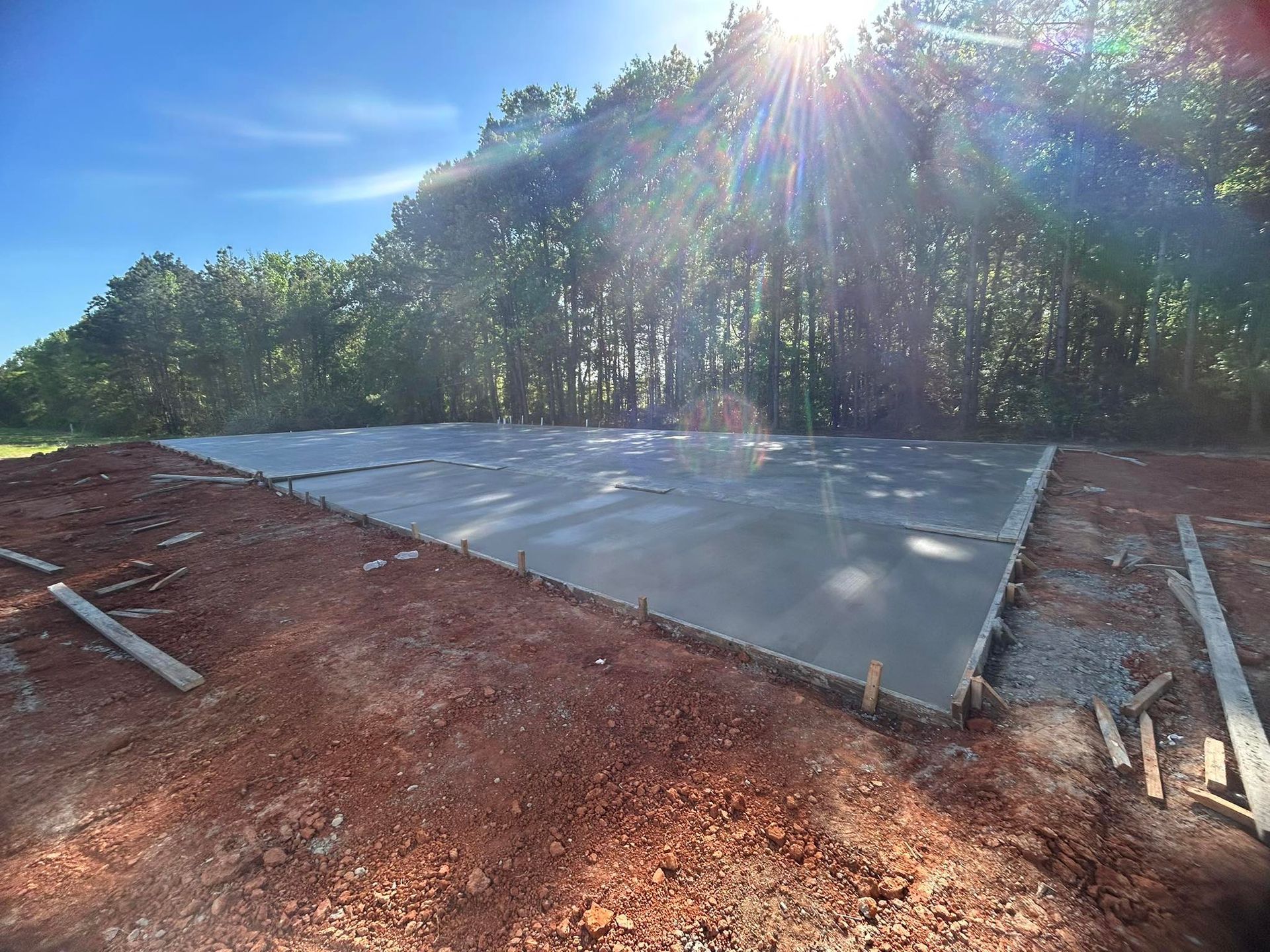 A concrete foundation is being built in a dirt field with trees in the background.
