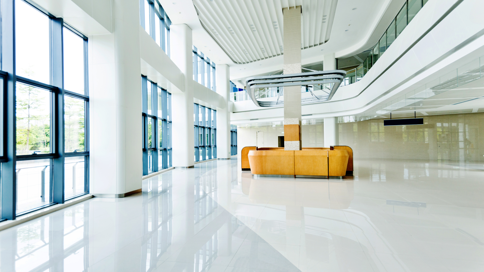 Bright, spacious modern lobby with large windows and polished white floor, curved front desk, and a column.