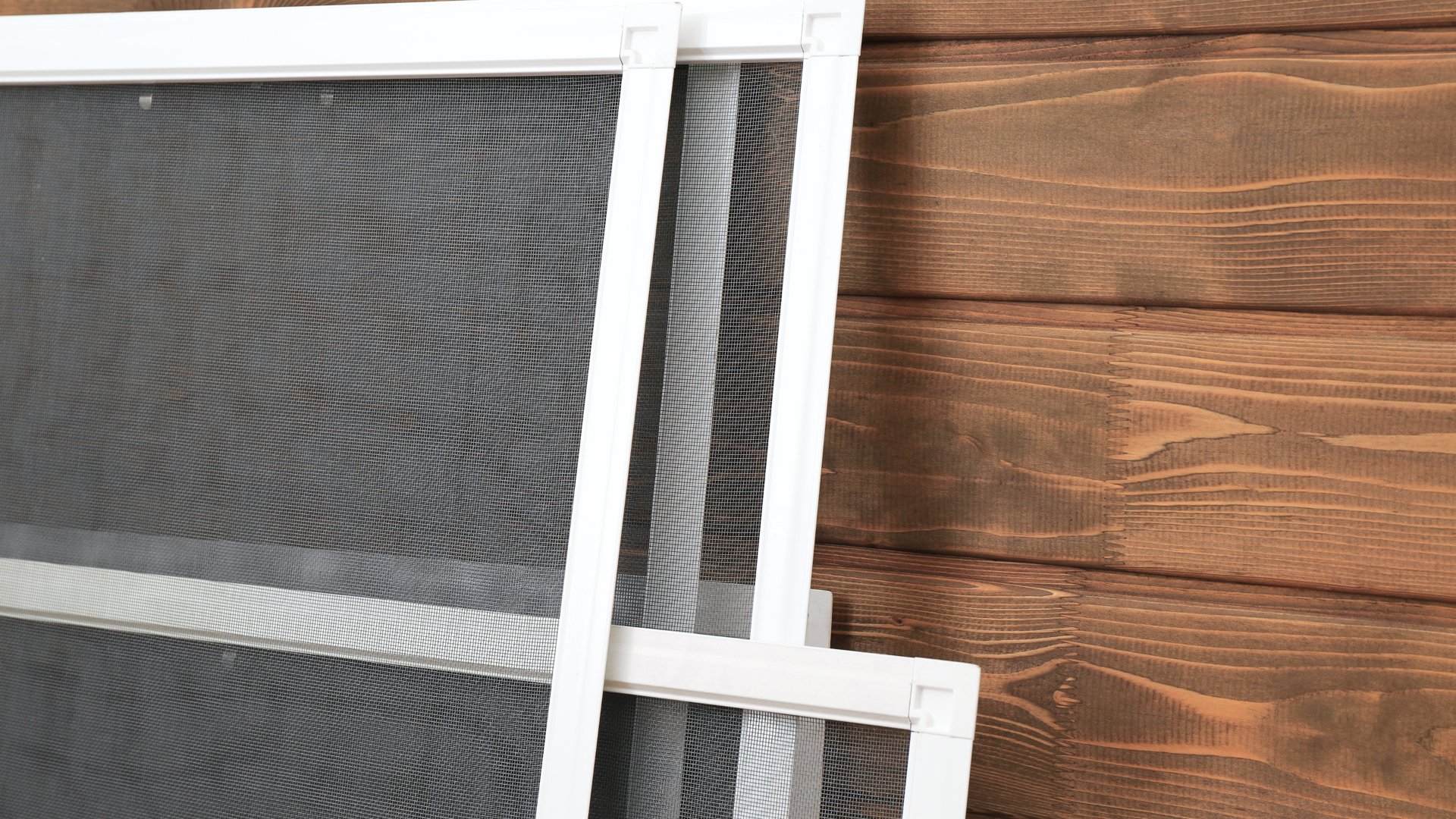 White-framed window screens stacked against a brown wooden wall.