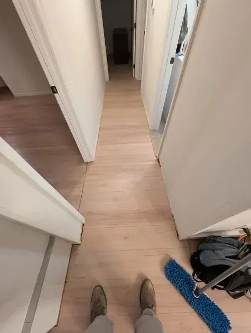 A person is standing in a hallway with a mop on the floor.