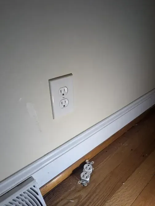 A white electrical outlet on a wall next to a fan.