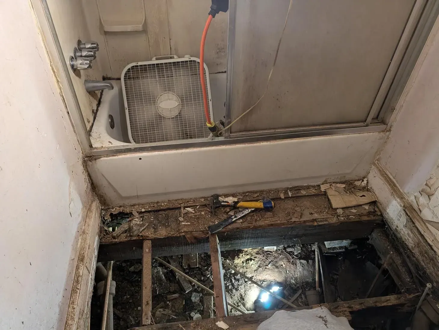 A bathroom with a bathtub and a fan on the floor.