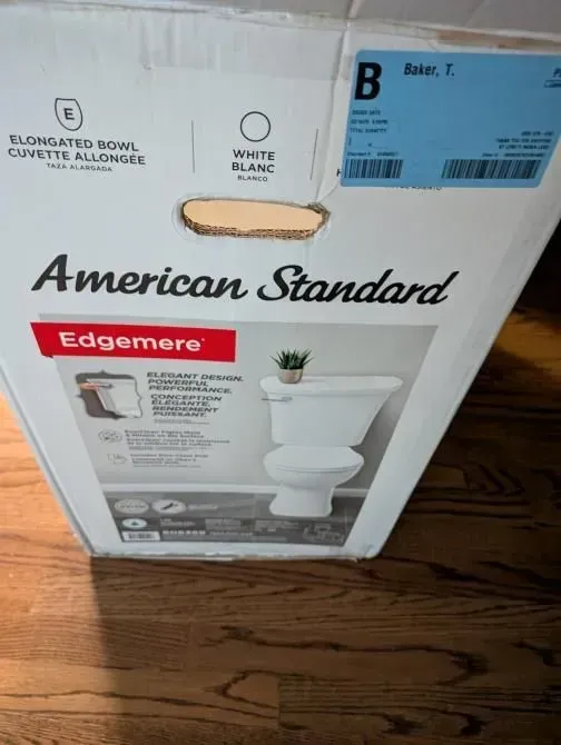 A box for an american standard toilet sits on a wooden floor