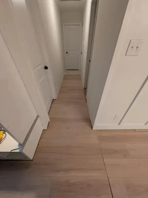 A long hallway with hardwood floors and white walls in a house.