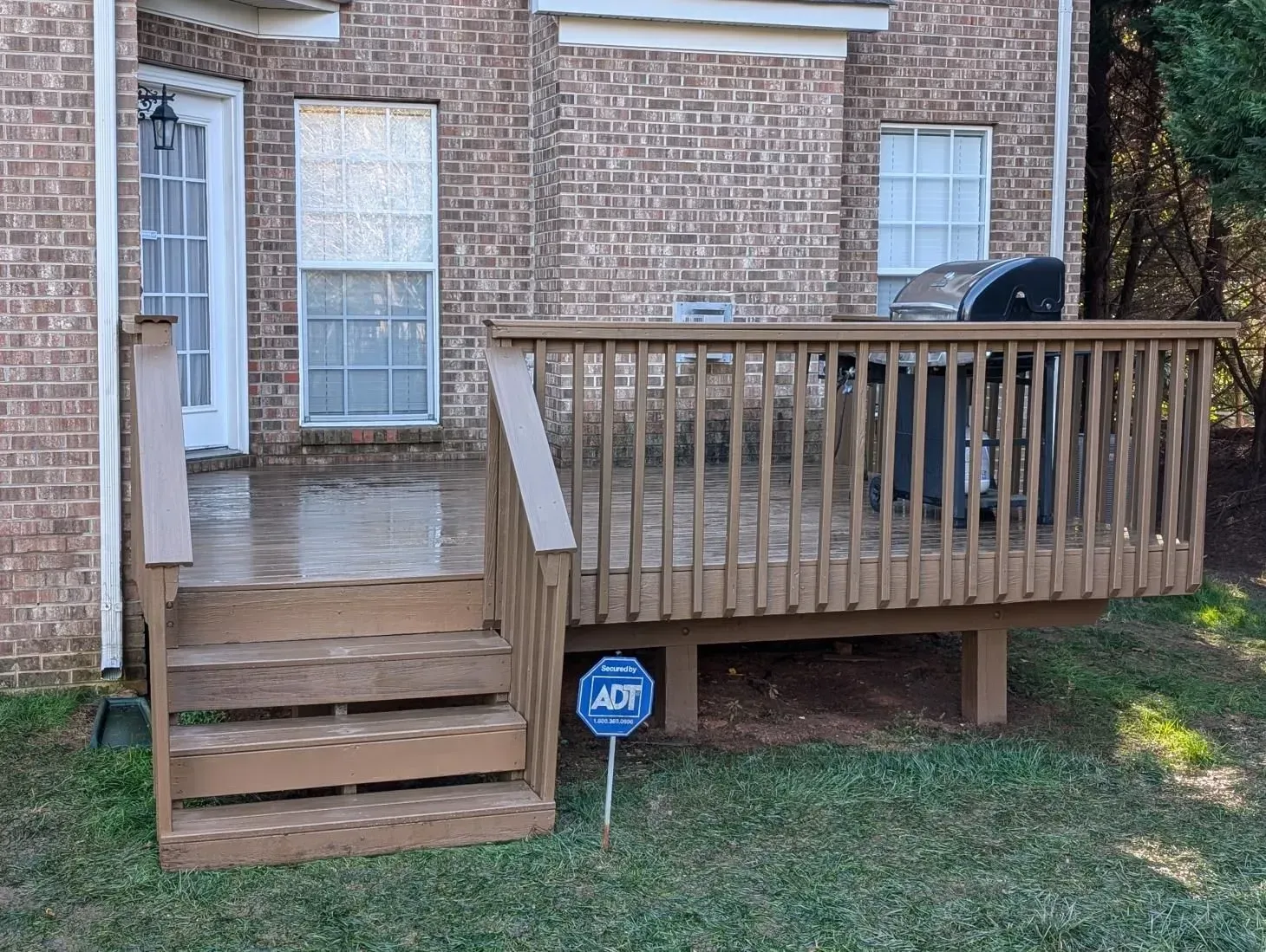 A wooden deck with stairs and a grill in front of a brick house.
