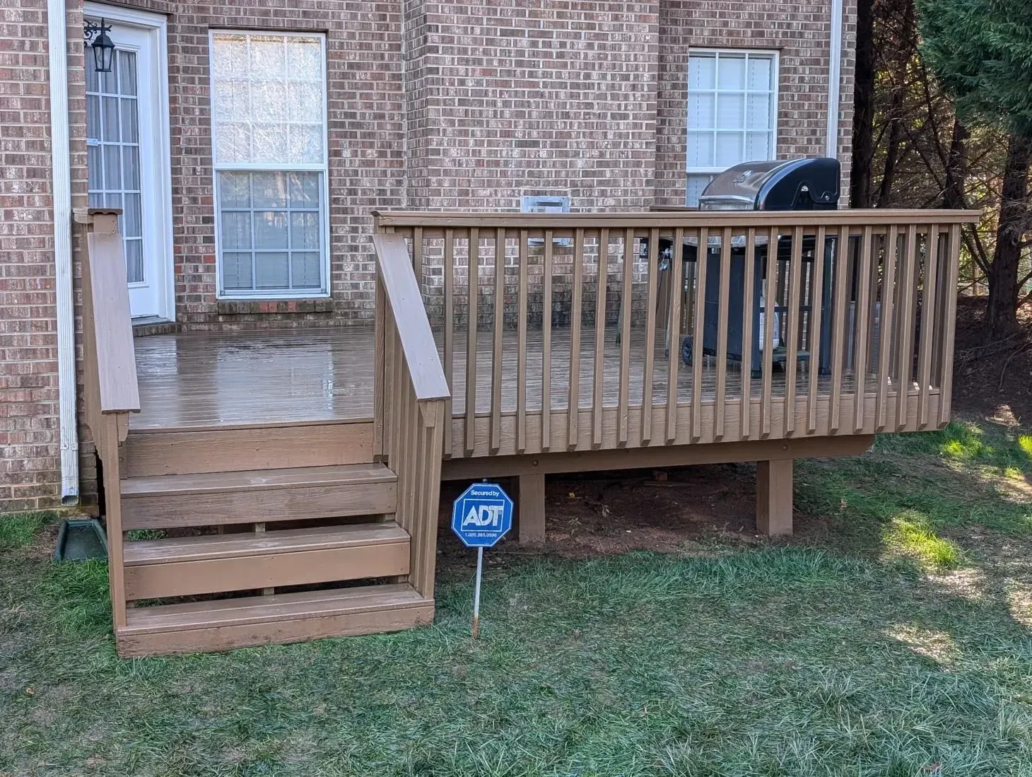 A wooden deck with stairs and a grill in front of a brick house.
