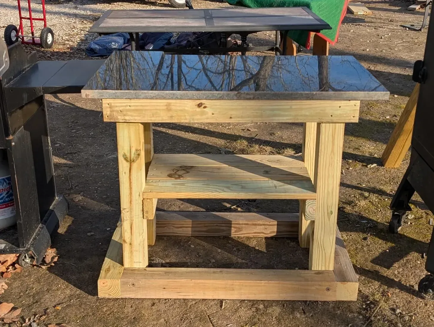 A wooden table with a stainless steel top is sitting on the ground.