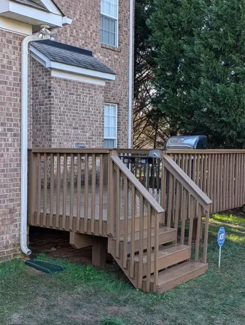 A wooden deck with stairs leading up to it is in front of a brick house.