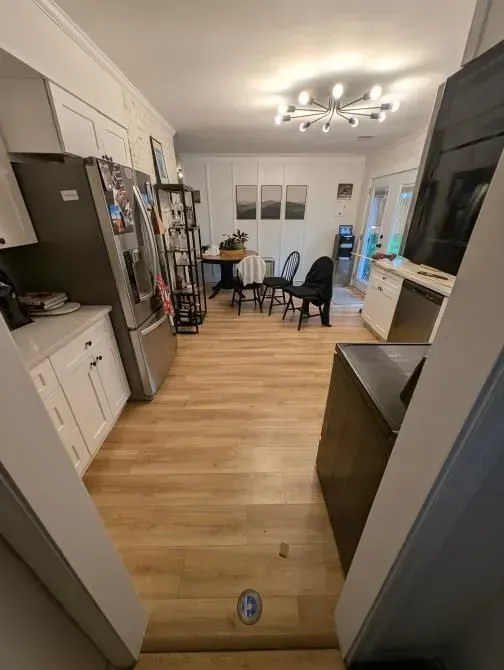 A kitchen with hardwood floors , a refrigerator , a table and chairs.