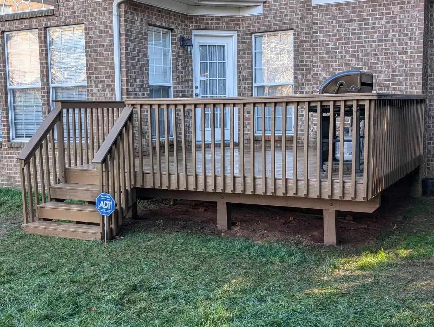 A wooden deck with stairs and a grill in front of a brick house.
