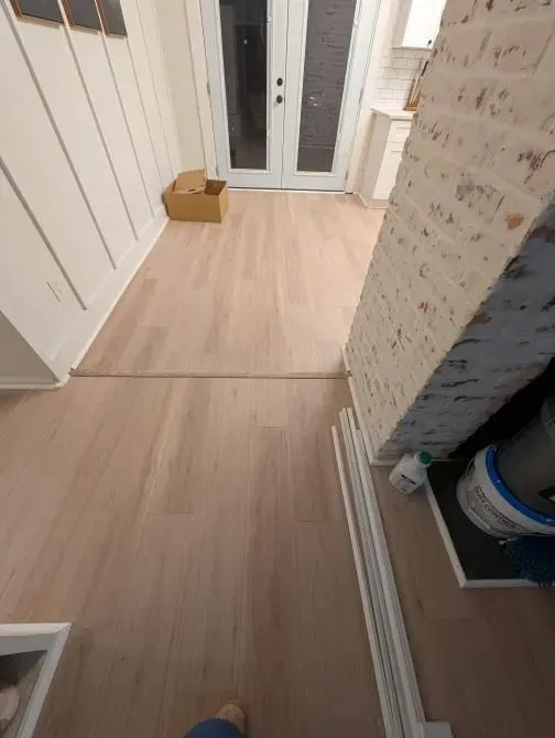 A person is standing on a wooden floor in a hallway.