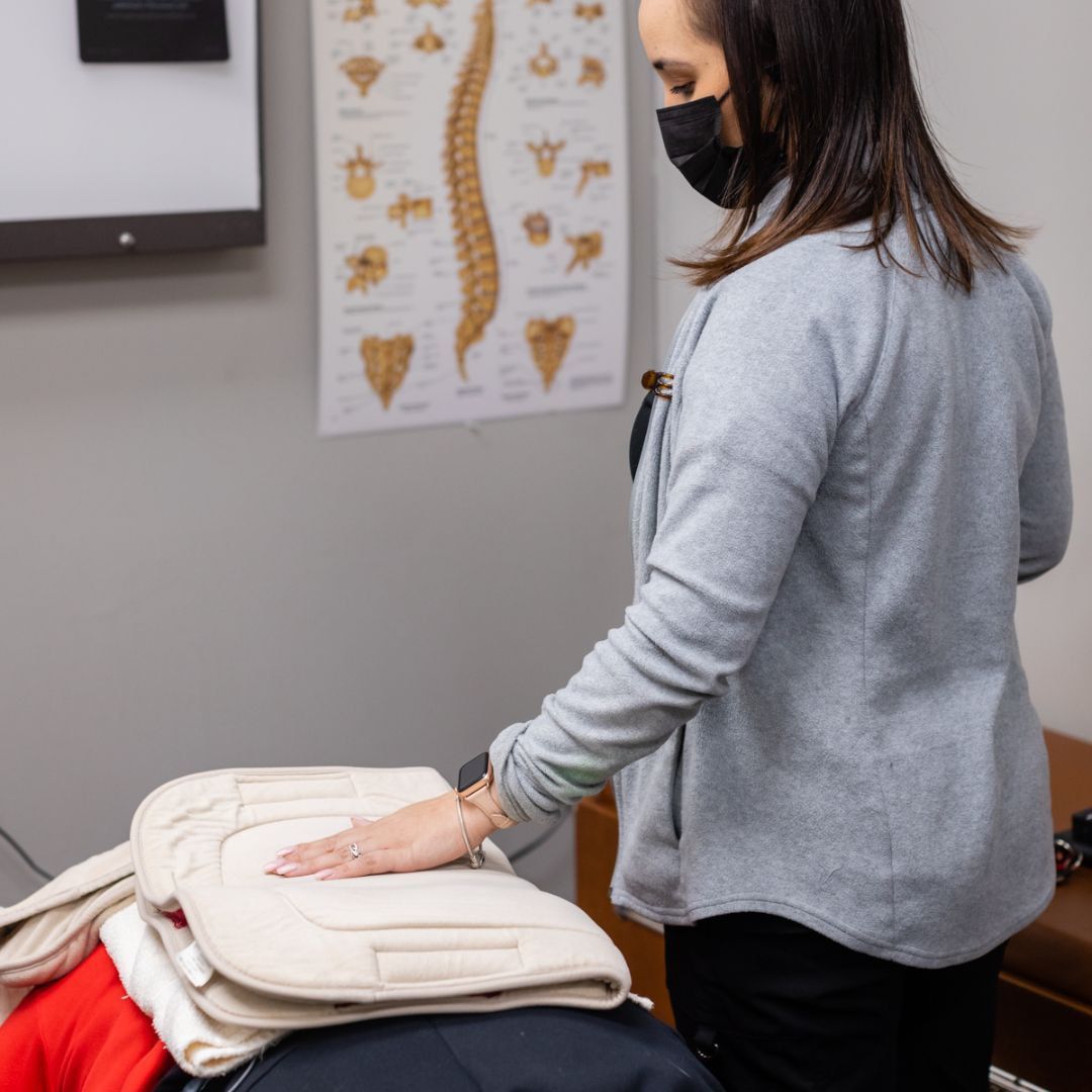 Woman in mask examining medical pads in an office; anatomical chart on wall.