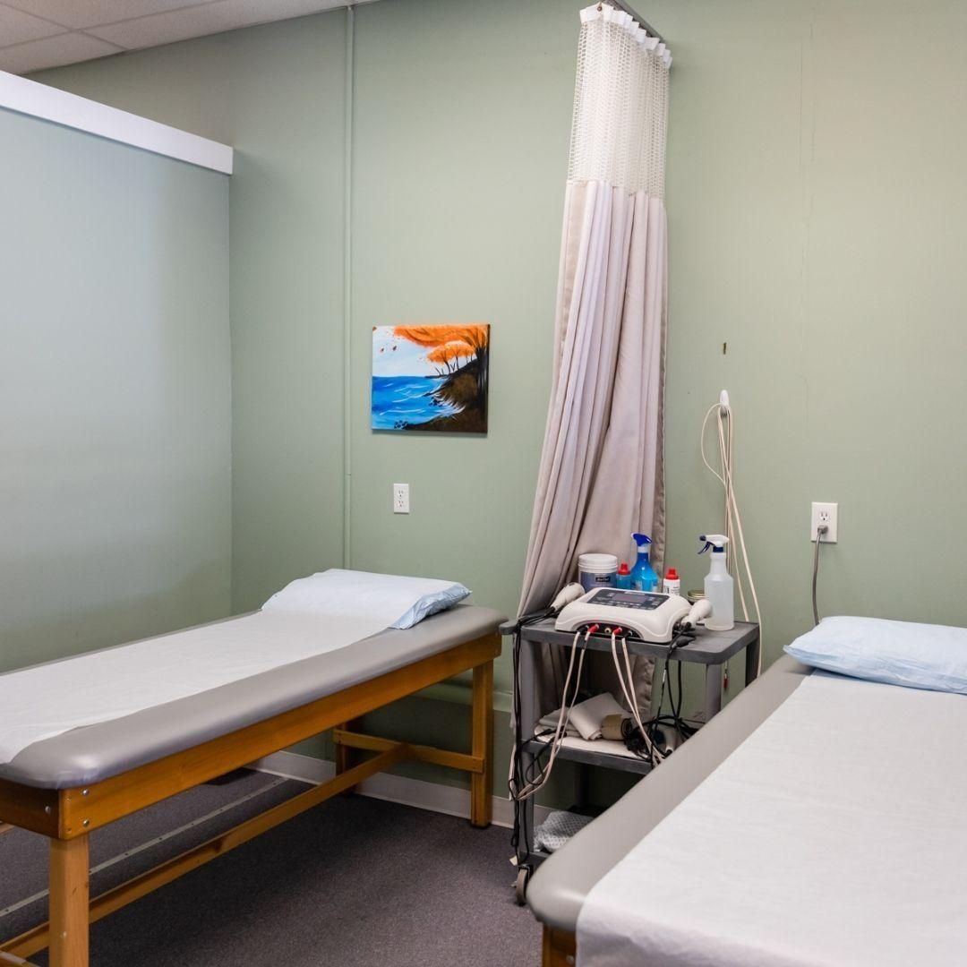 Medical exam room with two patient beds, equipment, and a painting on the wall.