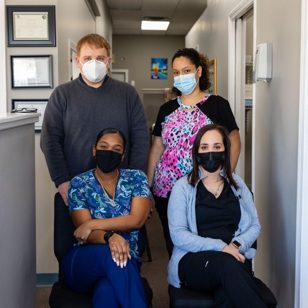 Four masked people pose in a medical office hallway.