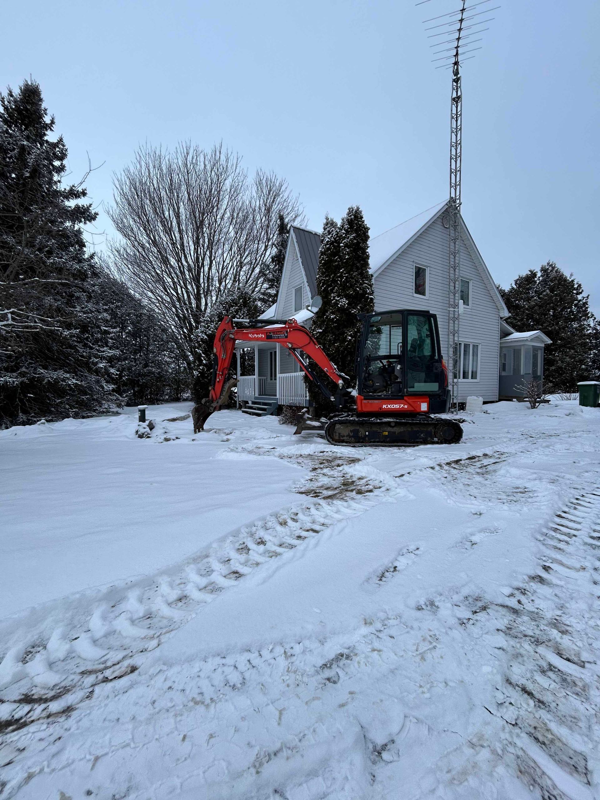 Une excavatrice est garée devant une maison sous la neige.
