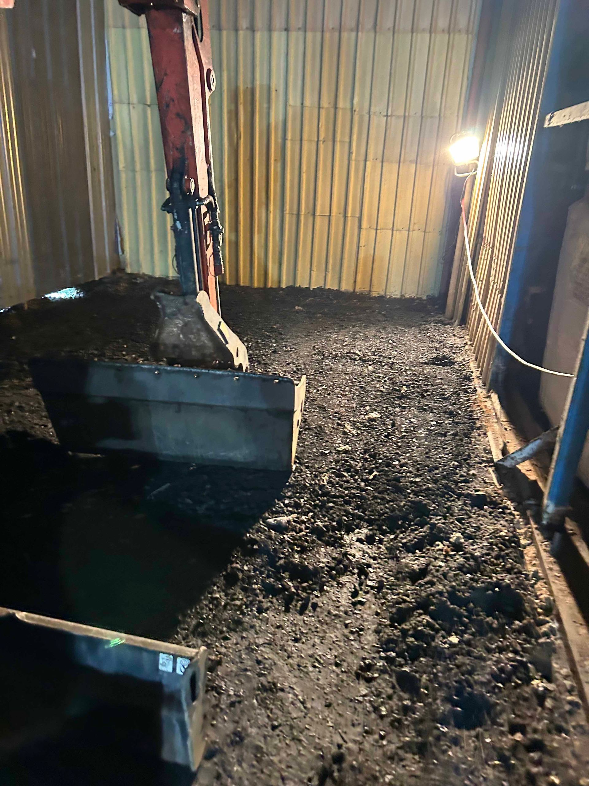 Une grande excavatrice creuse un trou dans le sol dans une pièce sombre.